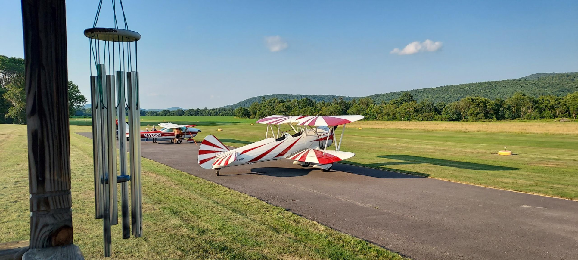 Red and white biplane on the ramp with another aircraft and wind chimes