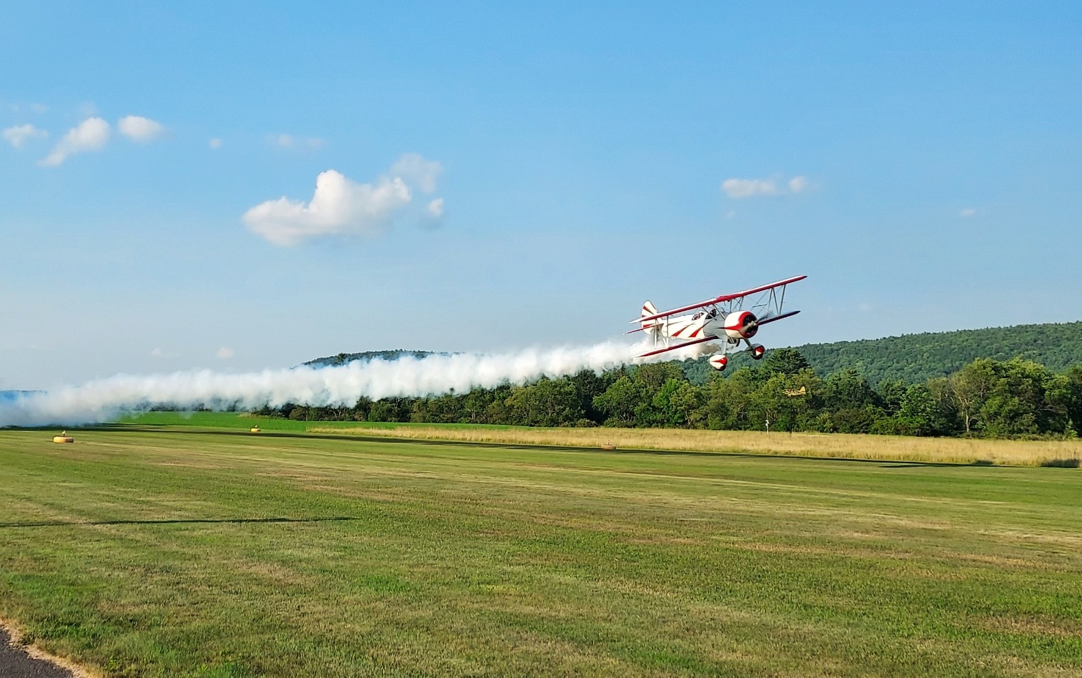 Red and white biplane flying low over the K23 grass airfield trailing smoke