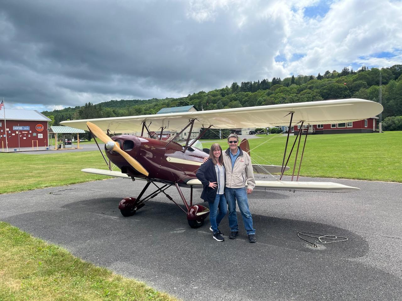 Couple posing with burgundy biplane on the ramp at K23