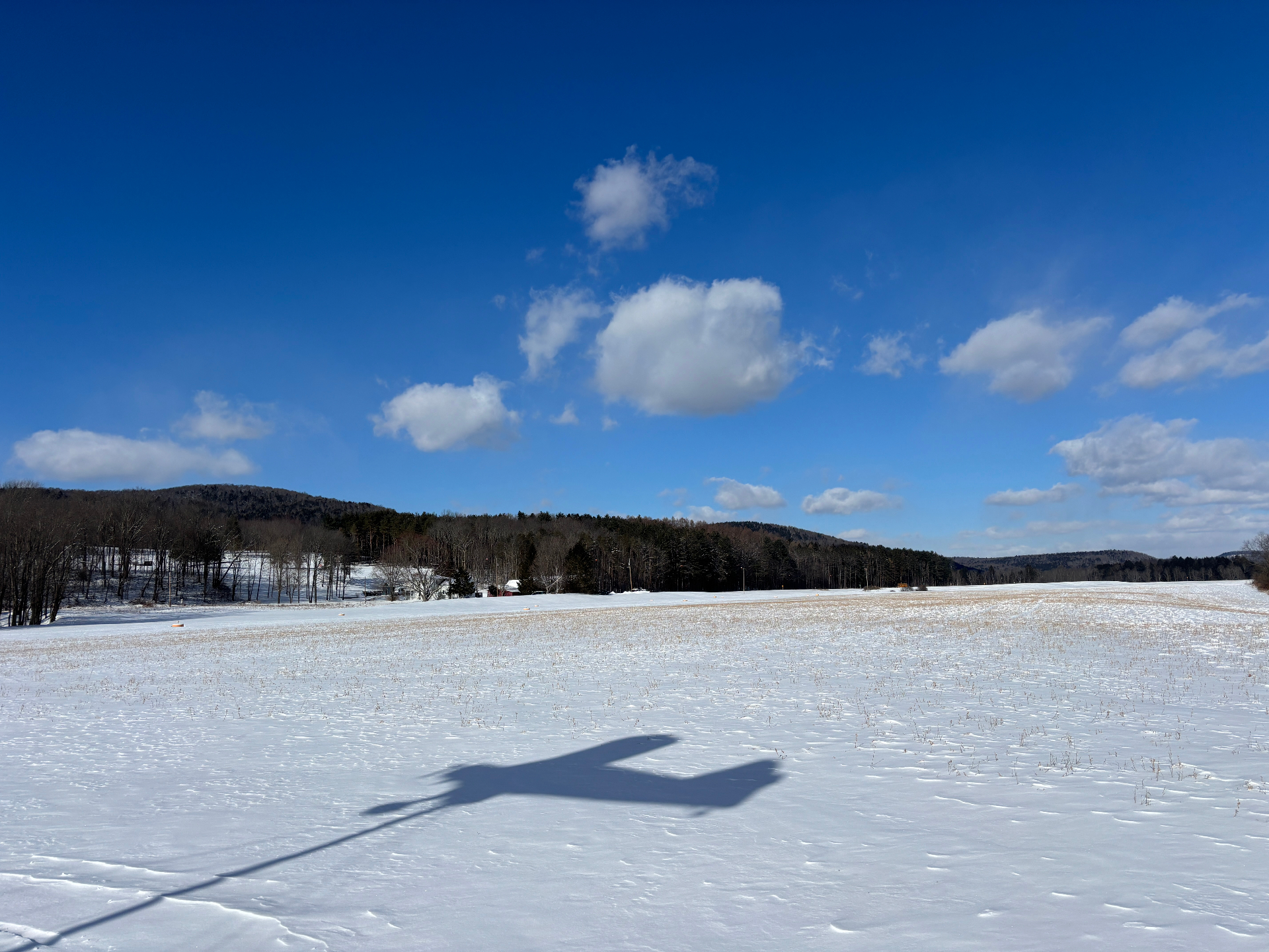 Snowy field with airplane shadow and hills in winter