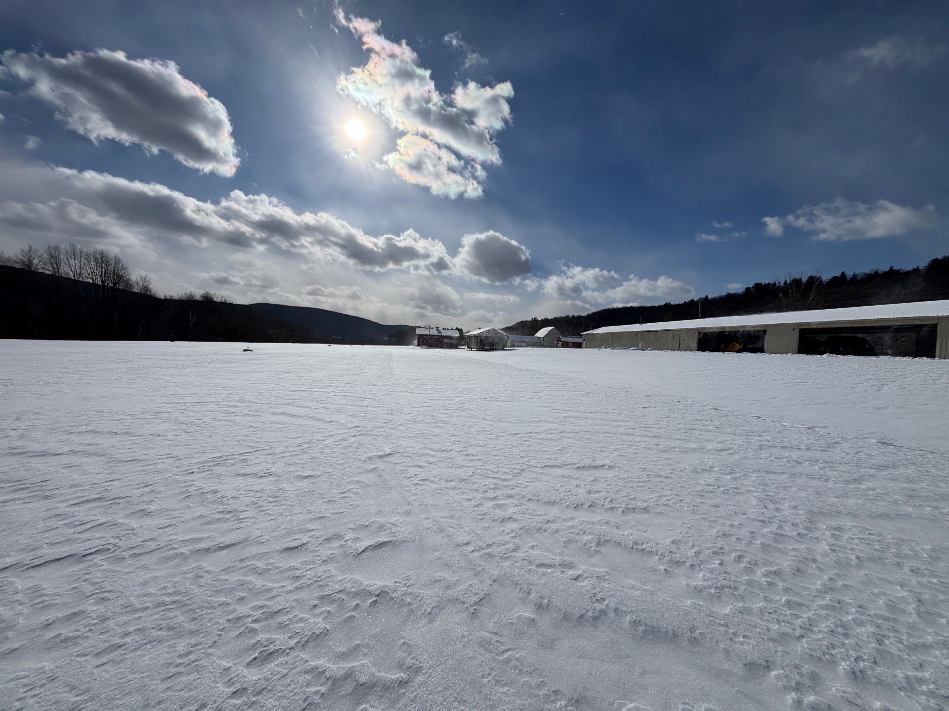 Snow-covered airfield with hangars and iridescent clouds in winter