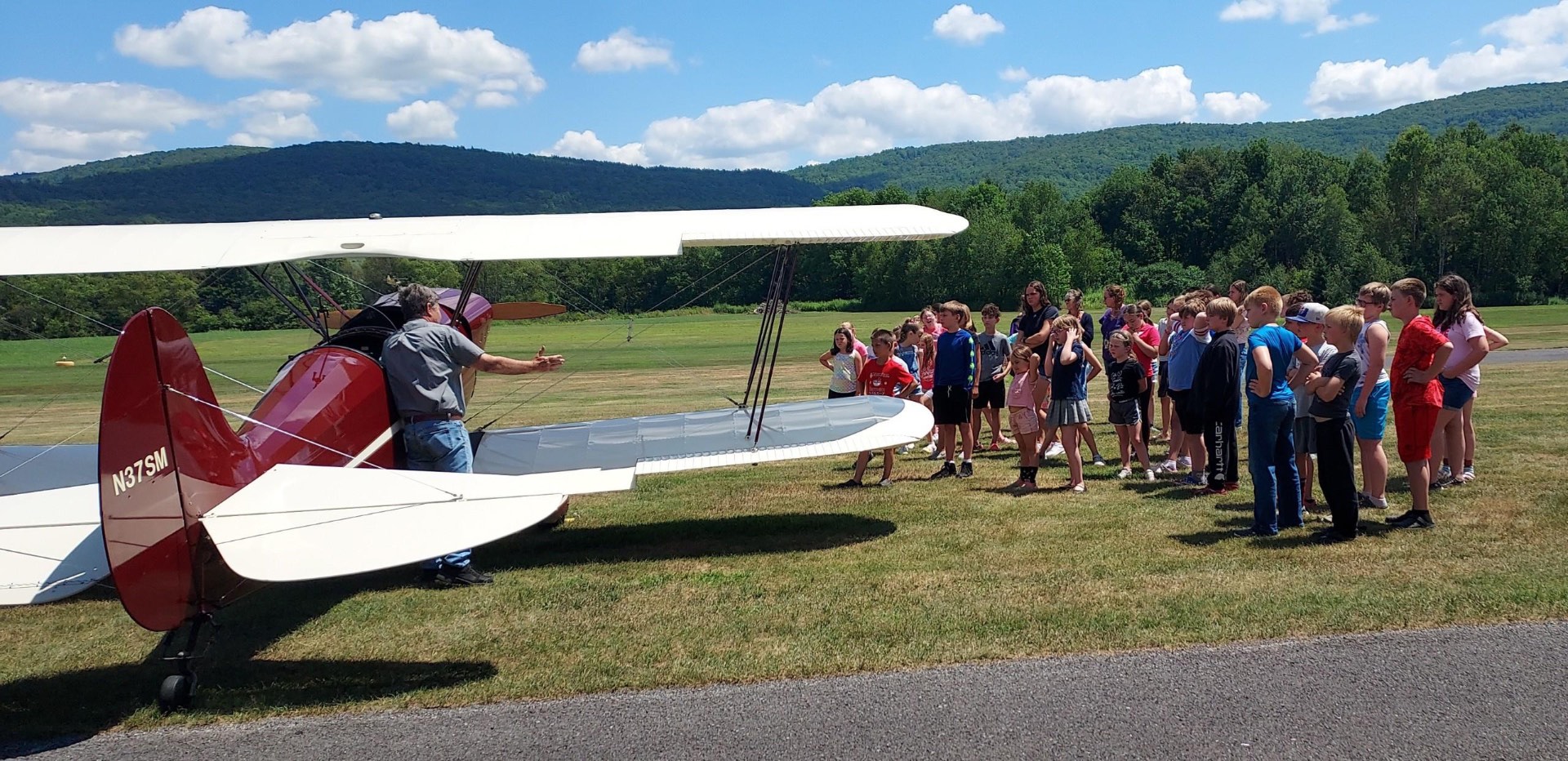Pilot showing a red and white biplane to a group of school children on the grass