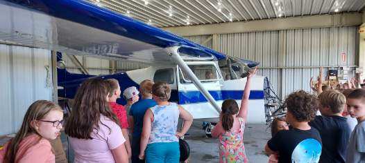 Children gathered around a blue and white Cessna inside the hangar
