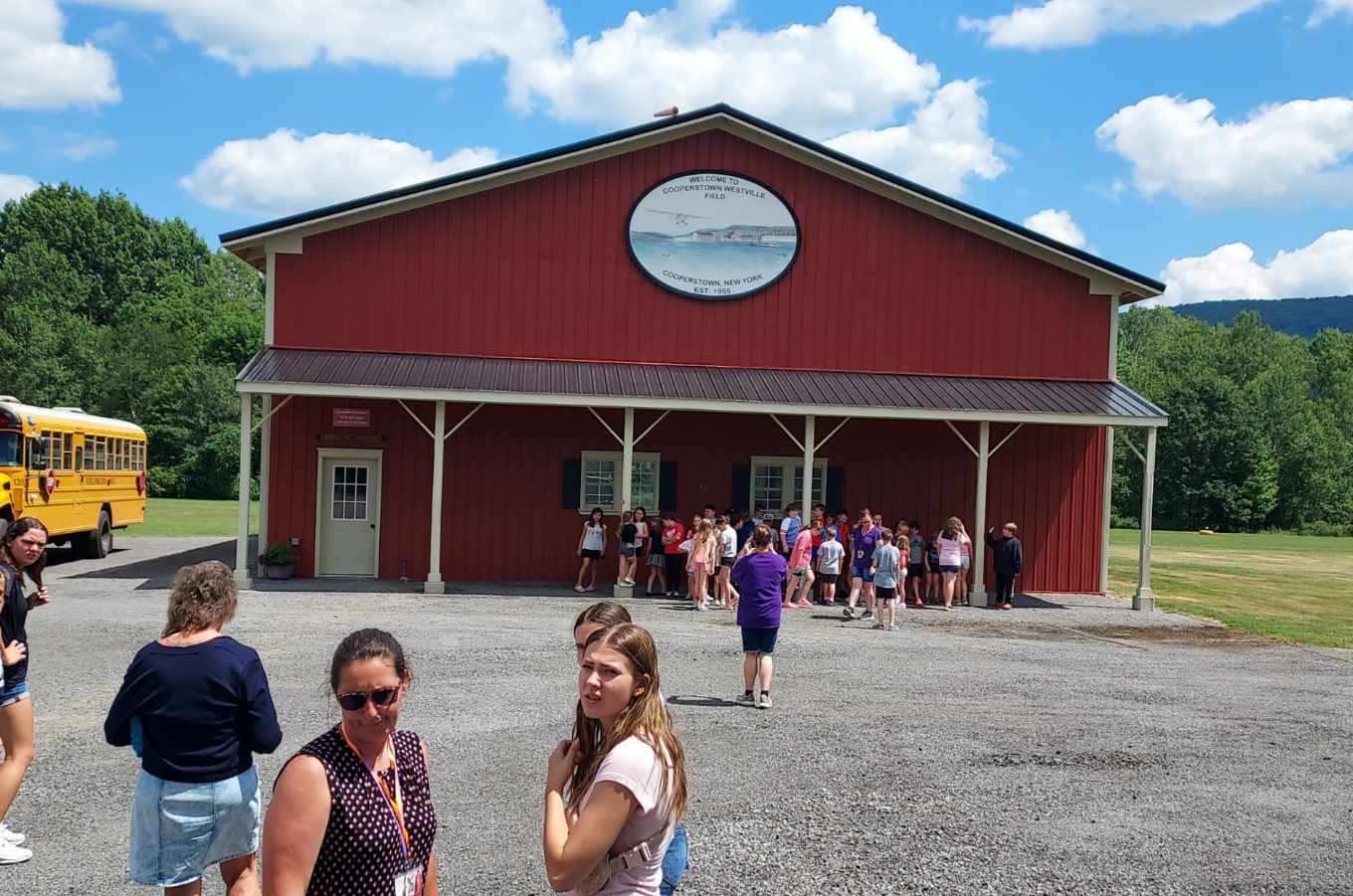 School group lined up under the porch of the red hangar with school bus and welcome sign